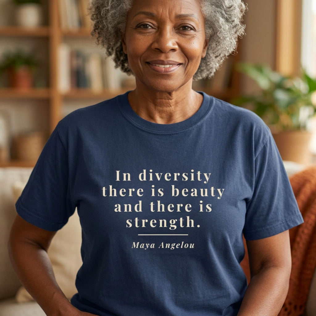 An older woman with short gray hair is seated indoors wearing a navy blue T-shirt with a white printed quote that reads, 'In diversity there is beauty and there is strength.' followed by 'Maya Angelou.
