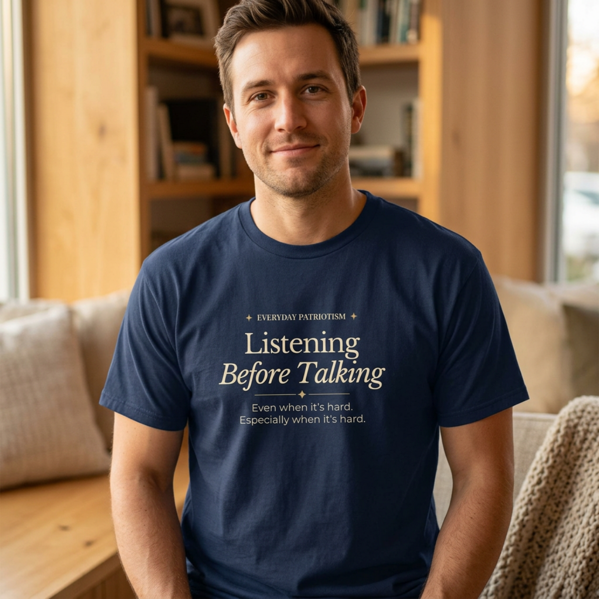 A man wearing a navy blue t-shirt with the text 'Listening Before Talking' printed in white on the chest, sitting in a cozy living room setting.